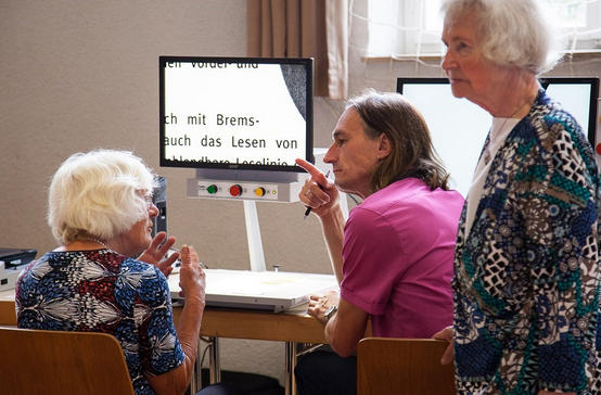 Drei Personen diskutieren vor einem Bildschirmlesegerät.